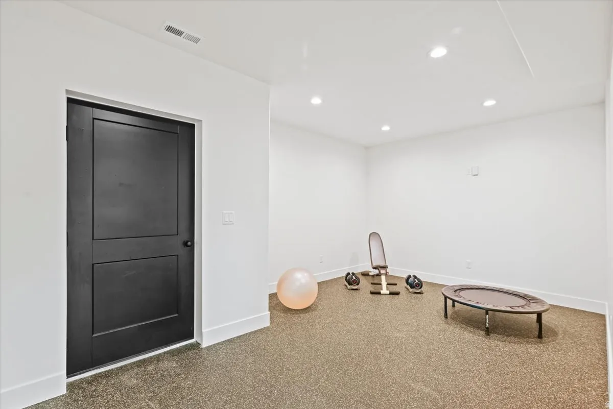 Versatile recreation room featuring recessed ceiling lighting, smooth drywall finishes, neutral carpet flooring, and a black six-panel solid-core door with contemporary hardware