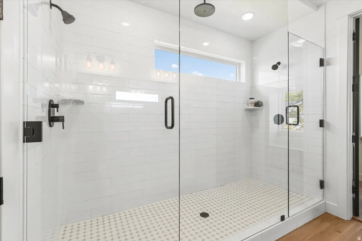 Glass-enclosed shower featuring white subway tile walls, a mosaic tile floor, dual shower heads, and matte black fixtures
