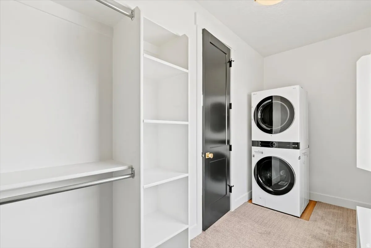 Dedicated laundry room featuring a stacked washer and dryer unit with modern controls, white framed glass-panel closet doors, neutral tile flooring, and ample wall space for storage and organization