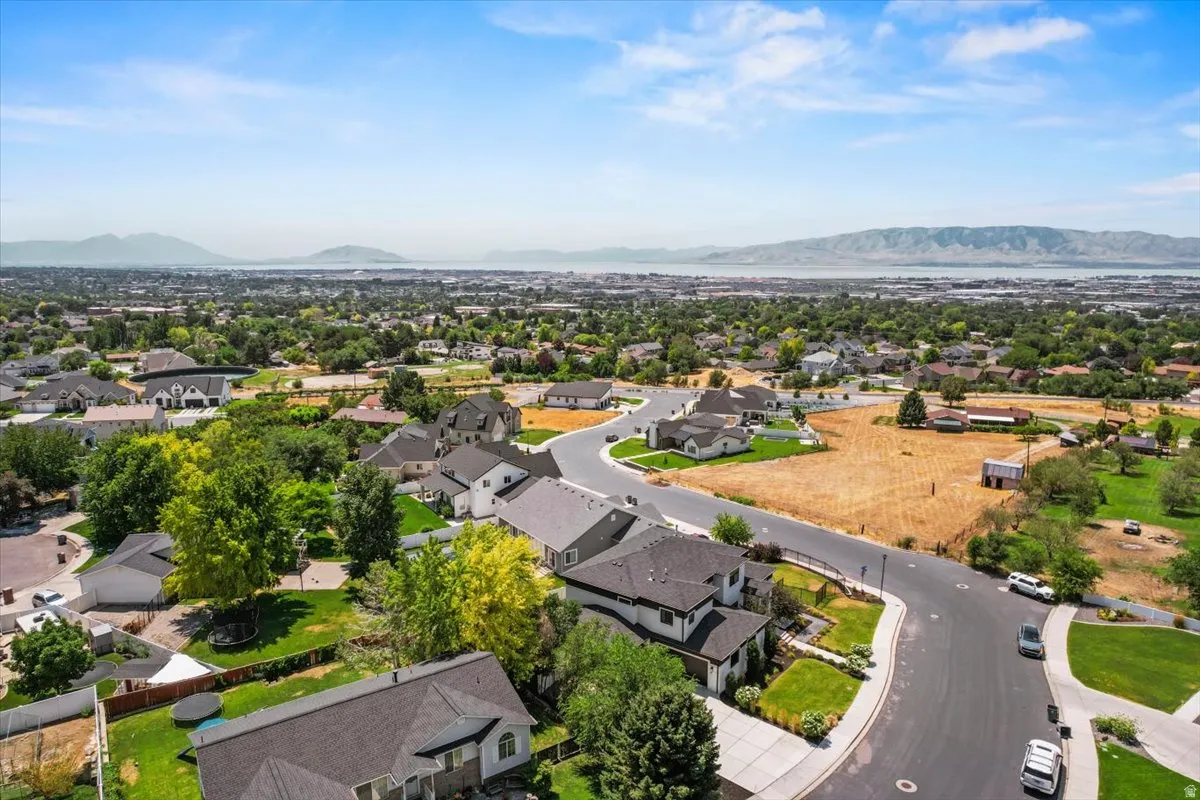 Aerial view showcasing a contemporary home with a curved driveway, dark architectural roofing, and manicured landscaping on an expansive lot