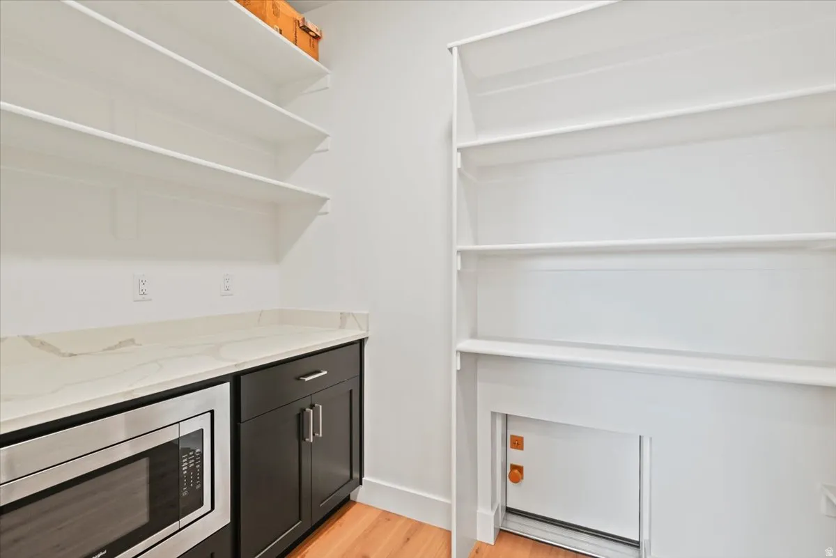 Kitchen pantry featuring extensive white shelving, a built-in stainless steel microwave, dark wood cabinetry, and a light-toned countertop