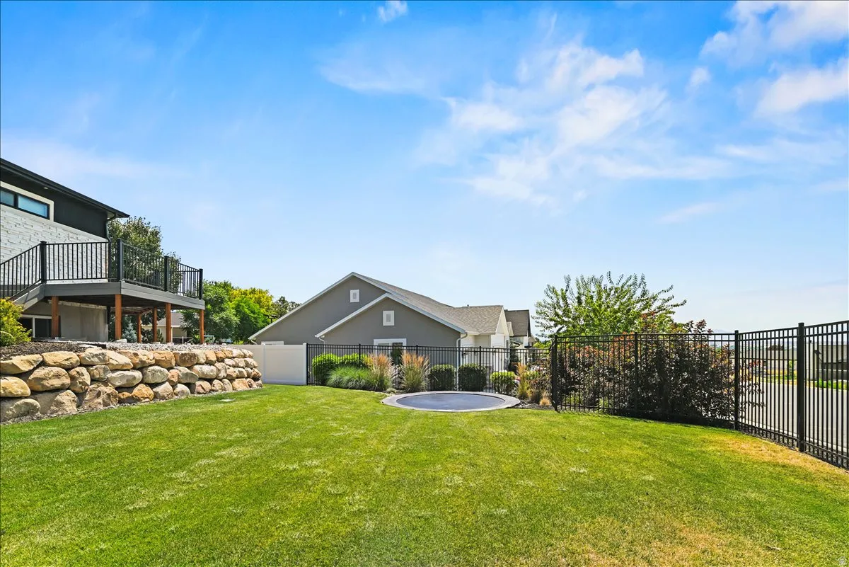 Expansive backyard oasis featuring a manicured lawn, in-ground swimming pool, wrought iron perimeter fencing, mature landscaping with natural stone retaining wall, and multi-level deck with upper-level access to the residence