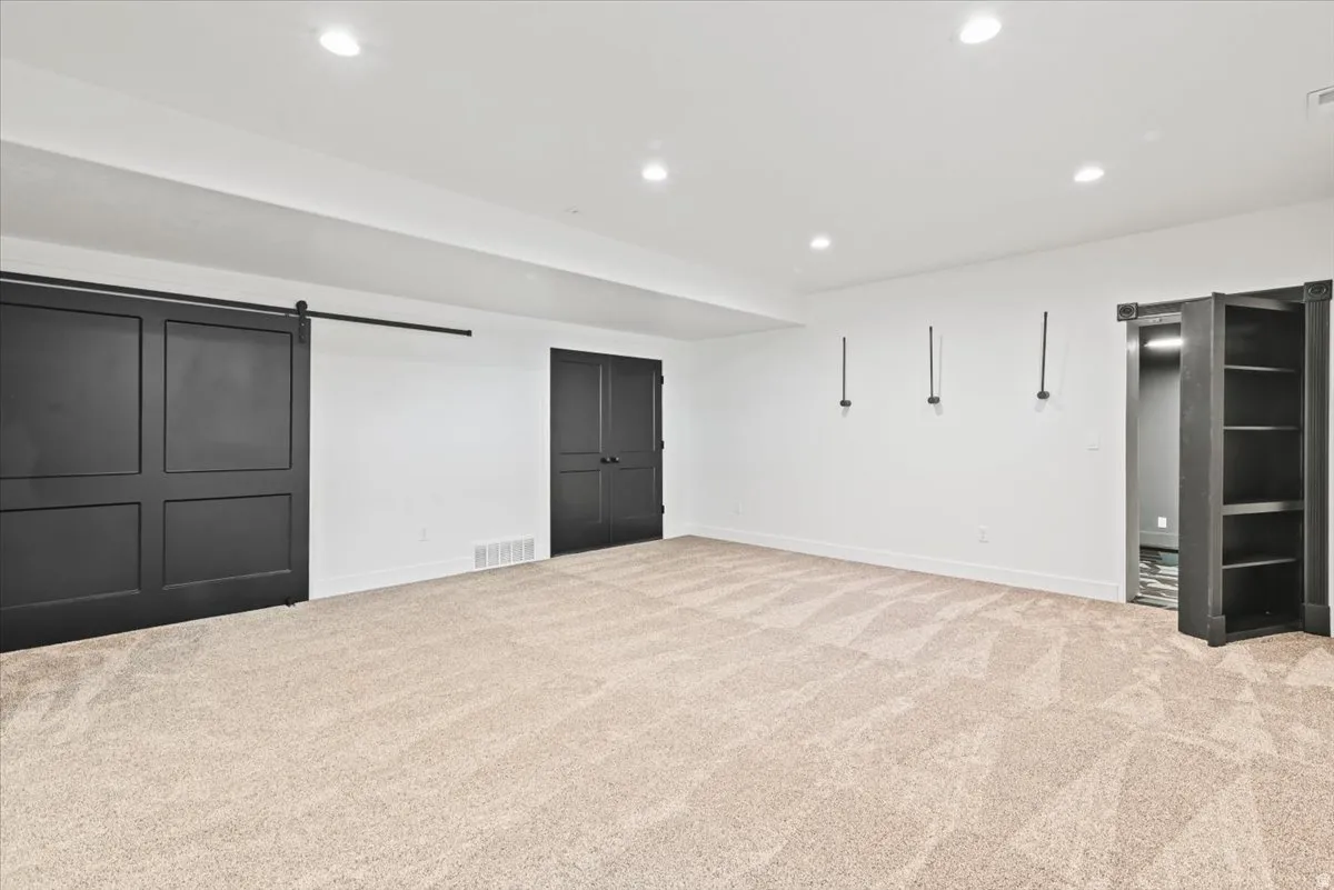 Spacious primary room featuring neutral carpet flooring, recessed ceiling lighting, and multiple entry points including sliding barn doors and glass-paneled French doors