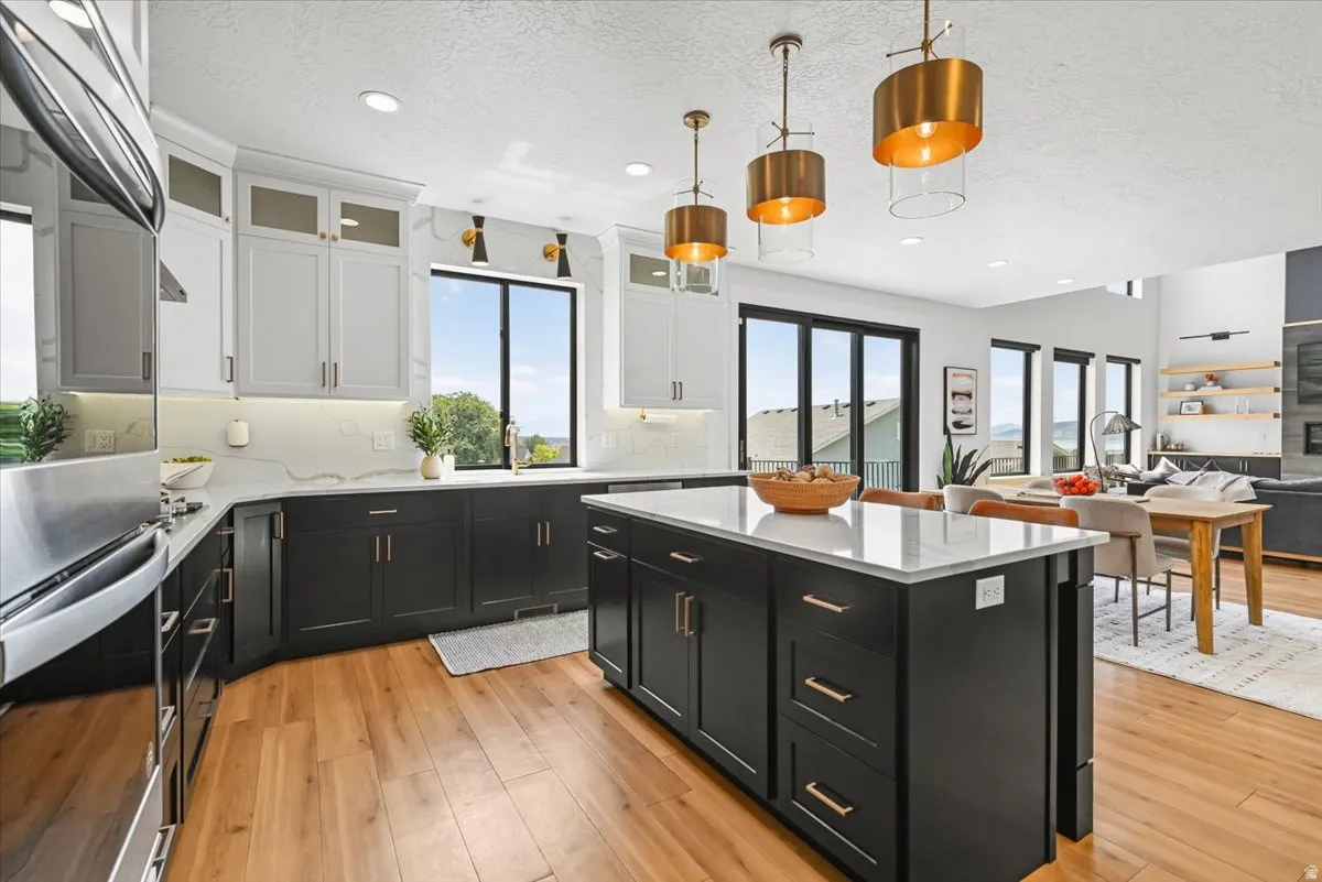 Sophisticated chef's kitchen featuring a two-tier island with waterfall edge countertop, contrasting cabinetry in white and charcoal with brushed brass hardware, stainless steel appliances, pendant lighting with brass accents, and wood-finish flooring thr