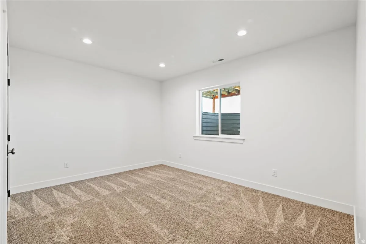 Bright bedroom featuring recessed ceiling lighting, neutral wall finishes, and neutral-tone carpeting with geometric pattern detailing