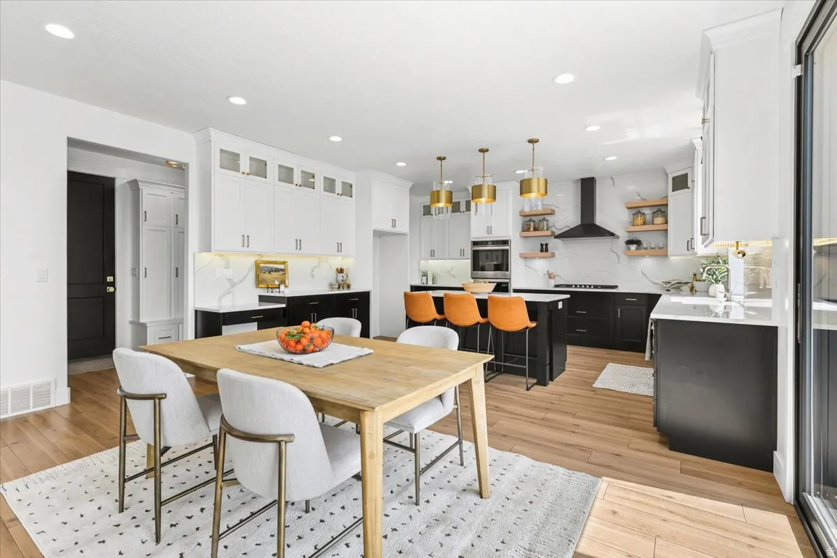 Open-concept kitchen and dining area featuring wood-finish flooring, white and black cabinetry, stone-finish countertops, and recessed lighting