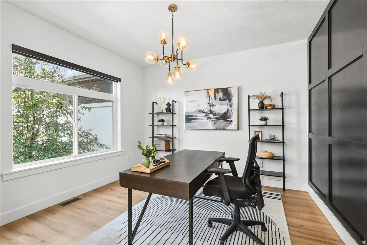 Sophisticated home office featuring a sleek black desk with tapered legs, ergonomic task chair, and warm wood-finish flooring