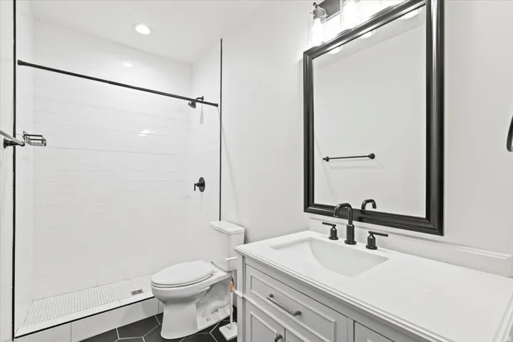 Modern bathroom featuring a white subway tile shower, clear glass enclosure, matte black fixtures, and a white vanity with a rectangular sink
