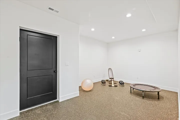 Versatile recreation room featuring recessed ceiling lighting, smooth drywall finishes, neutral carpet flooring, and a black six-panel solid-core door with contemporary hardware