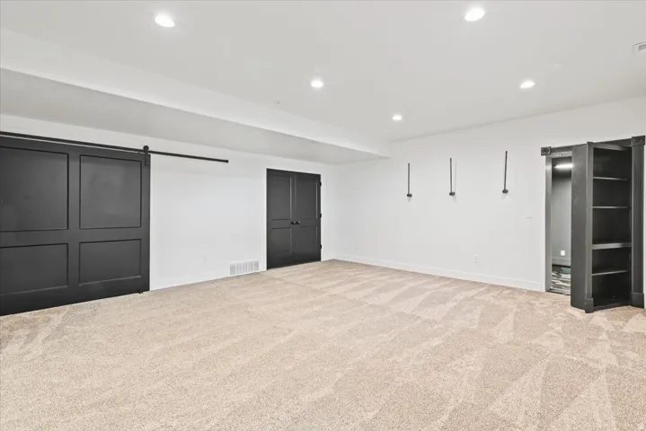 Spacious primary room featuring neutral carpet flooring, recessed ceiling lighting, and multiple entry points including sliding barn doors and glass-paneled French doors