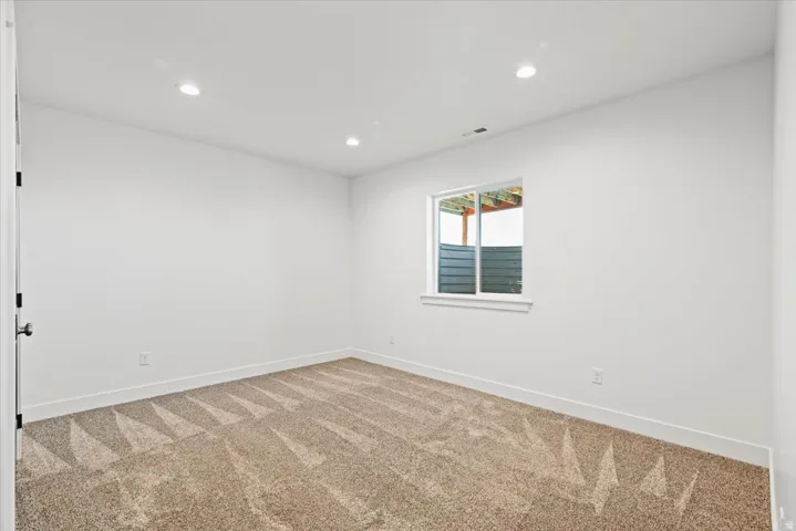 Bright bedroom featuring recessed ceiling lighting, neutral wall finishes, and neutral-tone carpeting with geometric pattern detailing