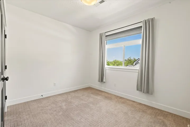Bright room featuring a large window, plush carpet flooring, white walls, and a ceiling light fixture