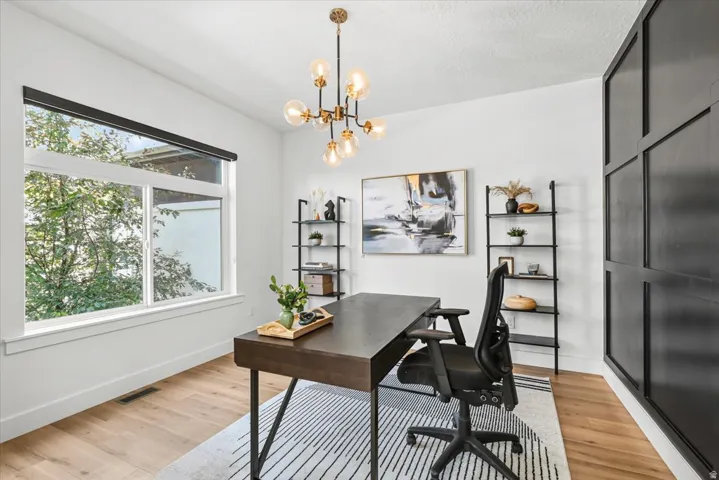 Sophisticated home office featuring a sleek black desk with tapered legs, ergonomic task chair, and warm wood-finish flooring