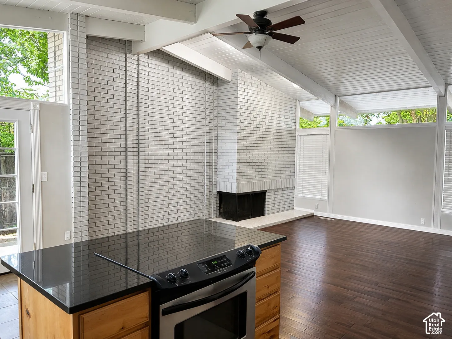 Vaulted ceilings with exposed beams, brick fireplace with hearth, wood-finish flooring, built-in range, and extensive window line