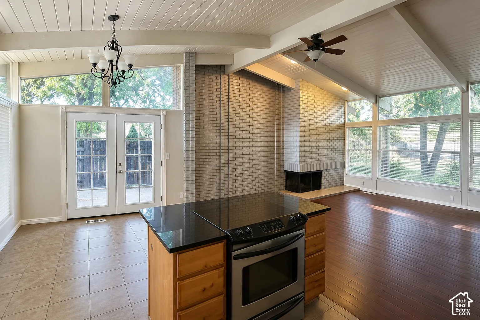 Vaulted ceiling with exposed beams, brick fireplace, wood-finish flooring, full-light French doors, and a kitchen island with built-in stainless steel appliances
