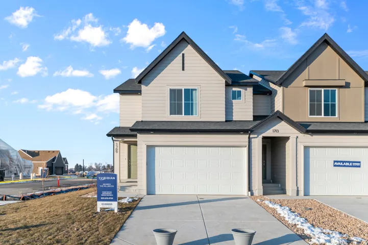 Modern townhome exterior featuring light-toned siding, dark roof shingles, and a prominent peaked entry