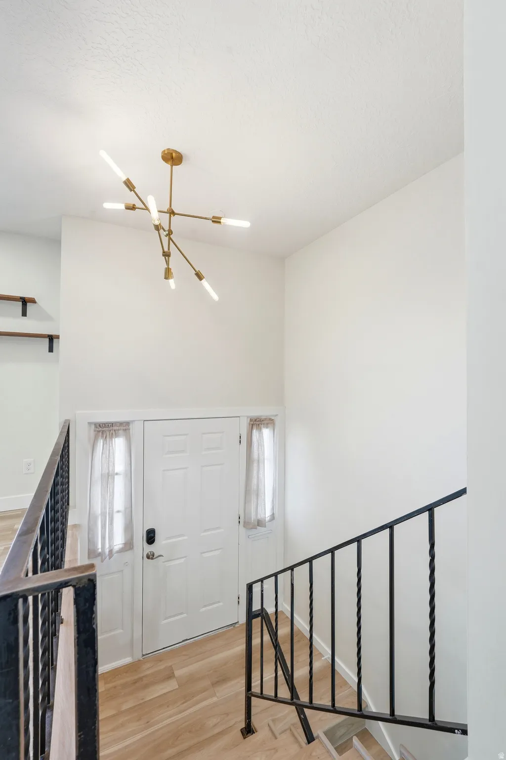 Bright upper-level hallway featuring a modern brass sputnik ceiling fixture, white six-panel double doors with satin nickel hardware, black metal stair railing with horizontal balusters, and warm wood-finish flooring throughout