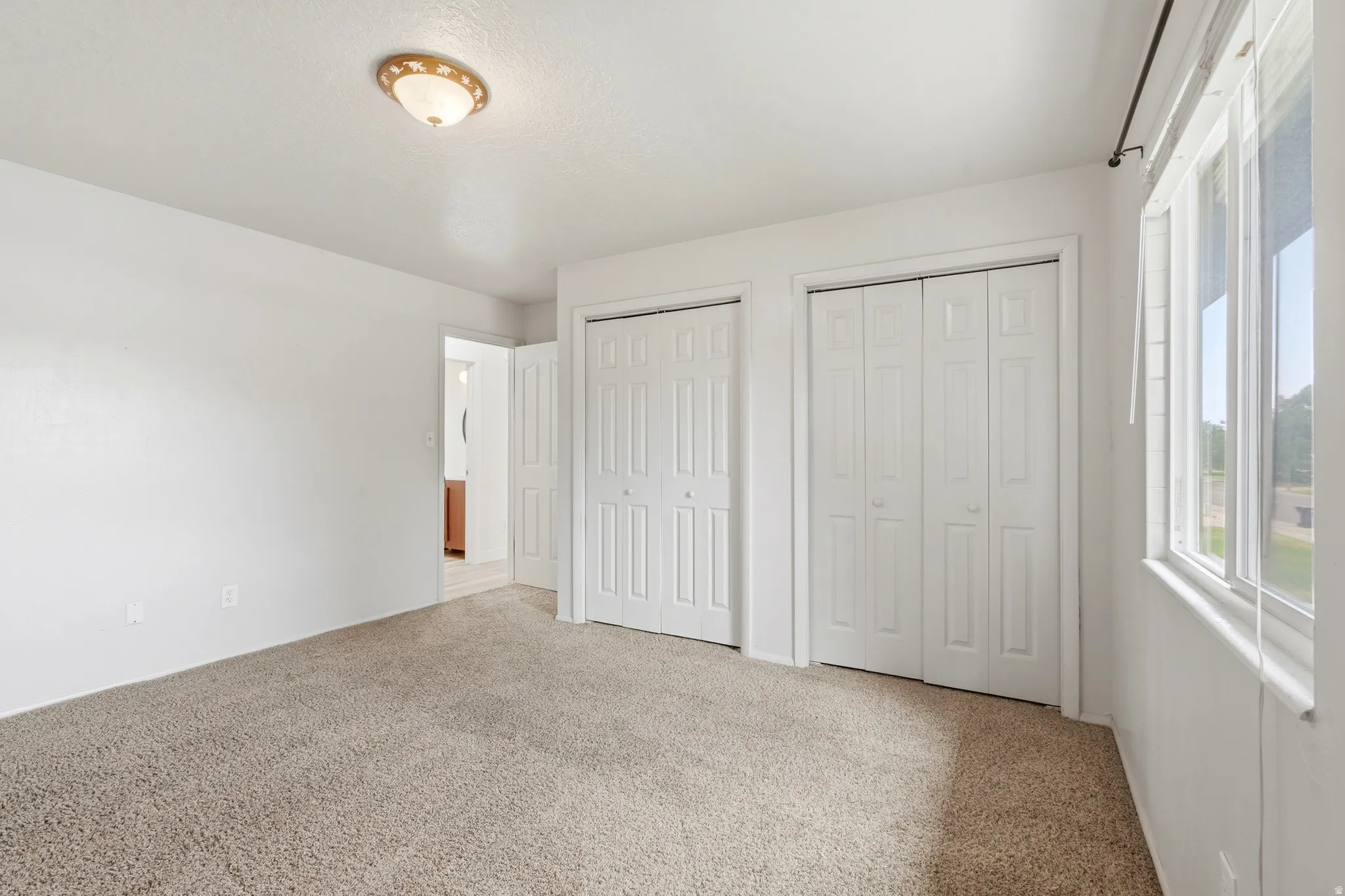 Carpeted room featuring dual bi-fold closet doors, a single window, and a flush mount ceiling light