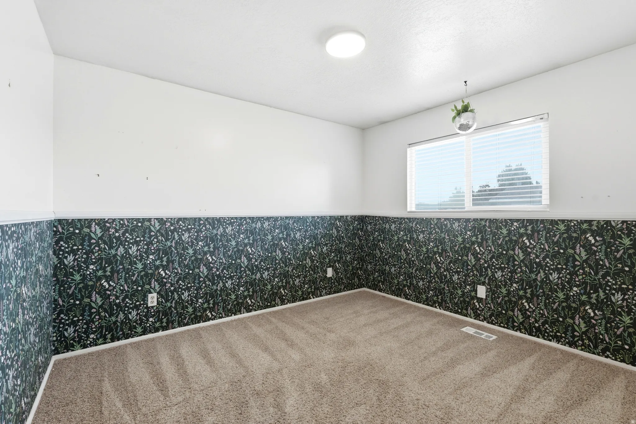 Room featuring two-tone walls with patterned wainscoting and white upper walls, light tan carpet, a rectangular window with horizontal blinds, and a flush-mount ceiling light
