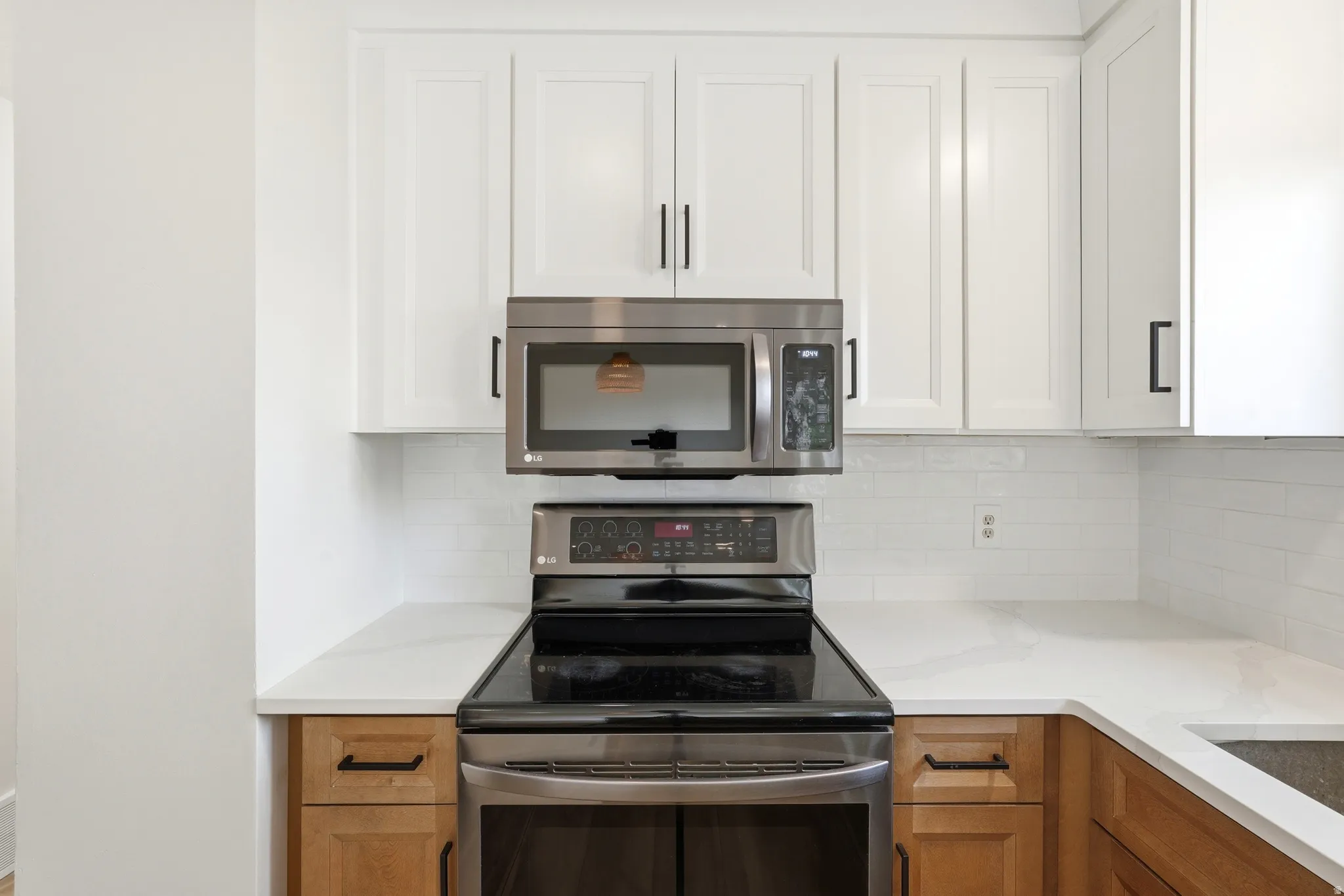 Kitchen featuring white upper cabinetry, wood-finish lower cabinetry, a white subway tile backsplash, light-toned countertops, and stainless steel appliances