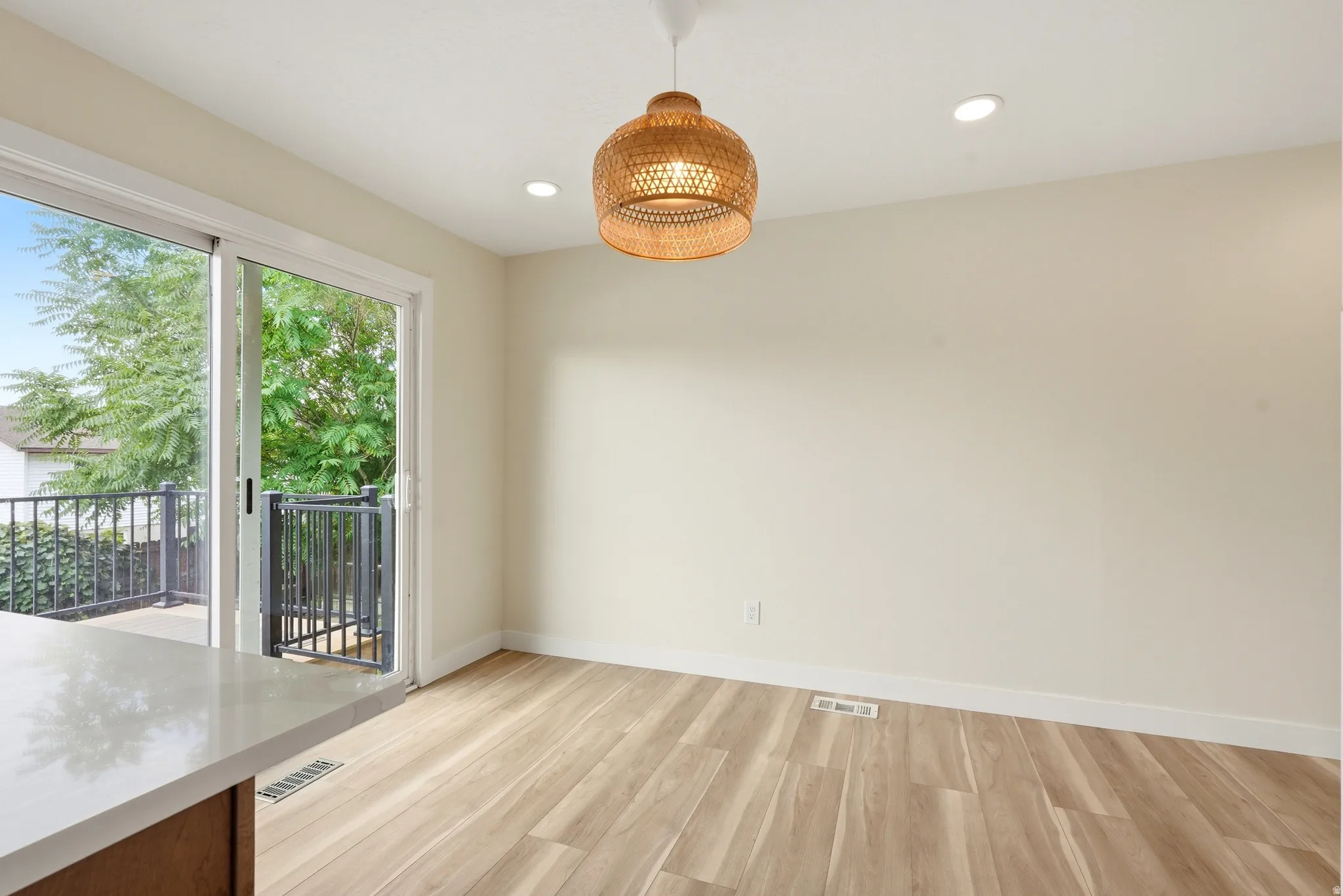 Spacious dining area featuring light wood-finish flooring, recessed lighting, and a woven pendant light fixture