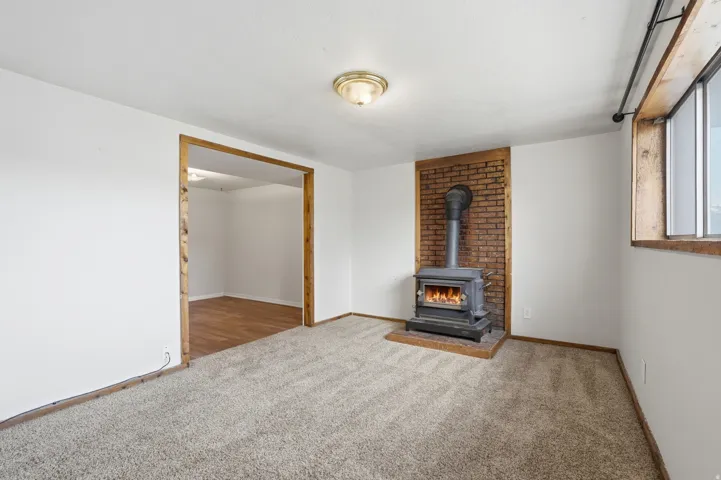 Room featuring a freestanding wood-burning stove with a brick surround, light-toned carpet, and an open doorway with wood trim