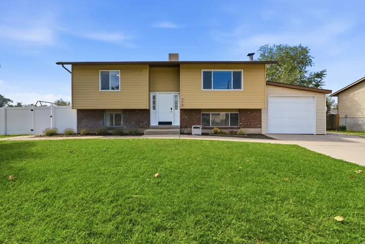 Split-level residence featuring a brick and siding exterior, an attached garage, a paved driveway, and a front lawn