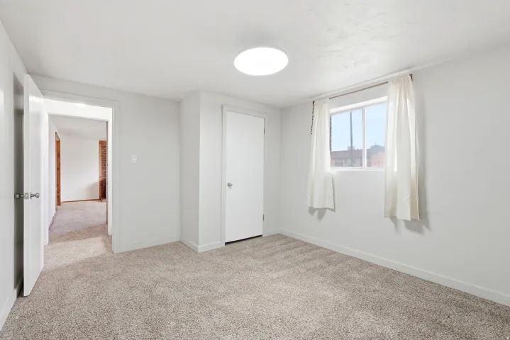 Carpeted room featuring a white ceiling-mounted light fixture, a window with white trim, and a white interior door