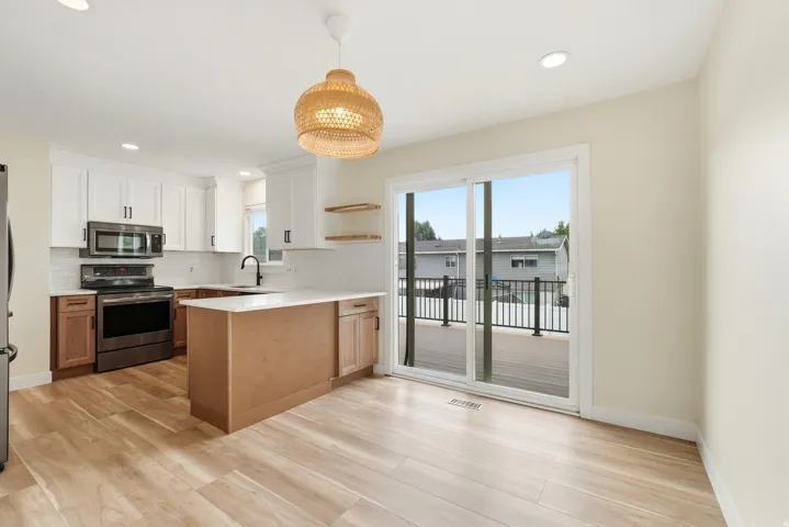 Open-concept kitchen with wood-finish flooring, a central island, stainless steel appliances, and white shaker cabinetry