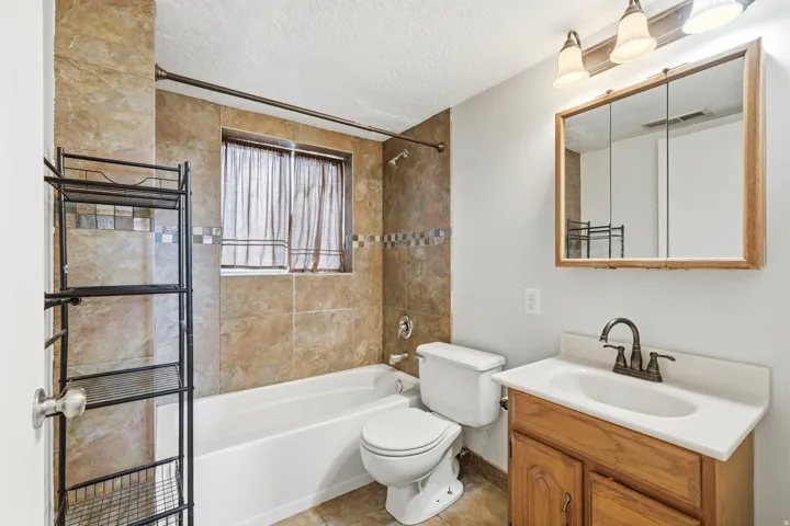 Bathroom featuring a built-in bathtub with a tile surround, a wood-finish vanity with a white countertop and integrated sink, a medicine cabinet with a wood-finish frame, and a three-light vanity fixture