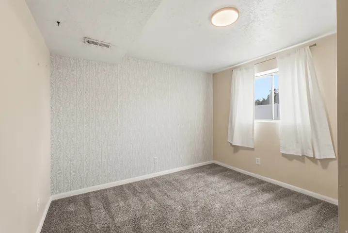 Carpeted room with a patterned accent wall, a single window, and an overhead flush-mount light fixture