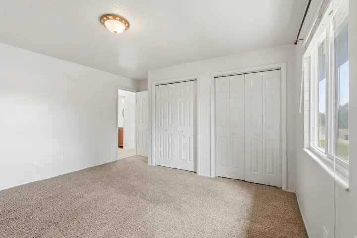 Carpeted room featuring dual bi-fold closet doors, a single window, and a flush mount ceiling light