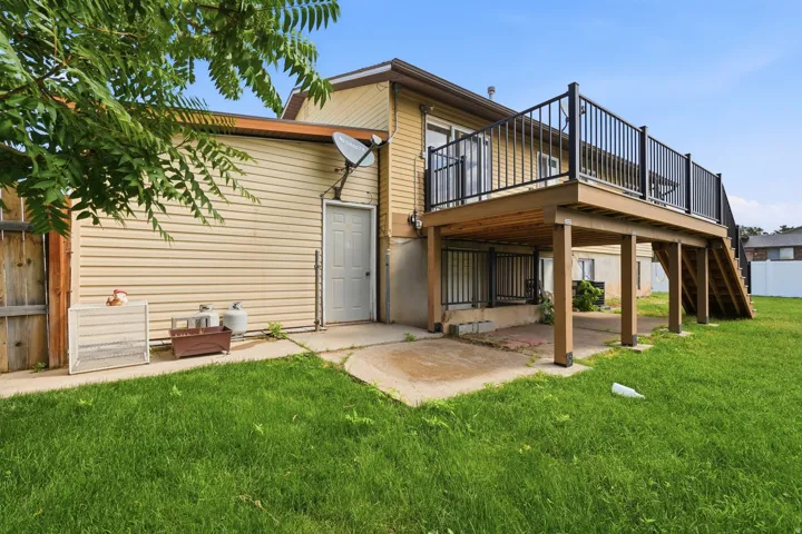 Rear exterior featuring a raised wood-finish deck with black railings, a ground-level concrete patio, and a grassy lawn