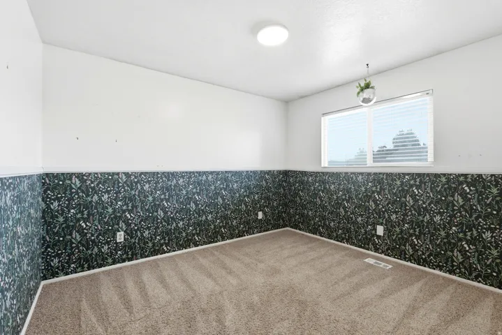 Room featuring two-tone walls with patterned wainscoting and white upper walls, light tan carpet, a rectangular window with horizontal blinds, and a flush-mount ceiling light