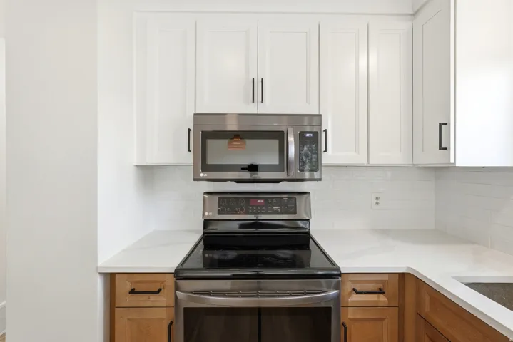 Kitchen featuring white upper cabinetry, wood-finish lower cabinetry, a white subway tile backsplash, light-toned countertops, and stainless steel appliances