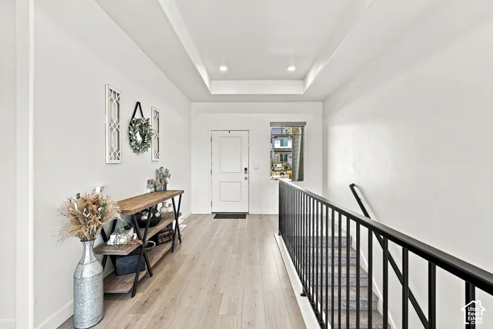 Entryway featuring light wood-finish flooring, a white paneled entry door, a tray ceiling with recessed lighting, and a black metal stair railing
