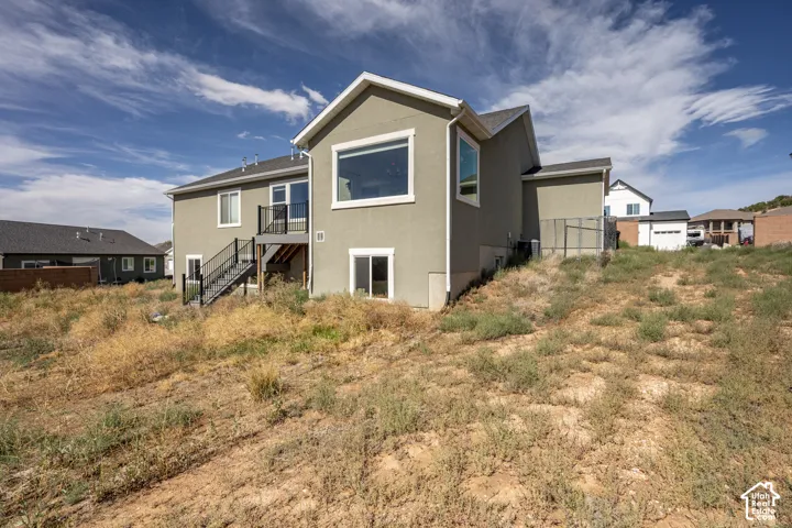 Contemporary stucco exterior featuring a second-story deck with dark railings, a prominent picture window, and a ground-level sliding glass door
