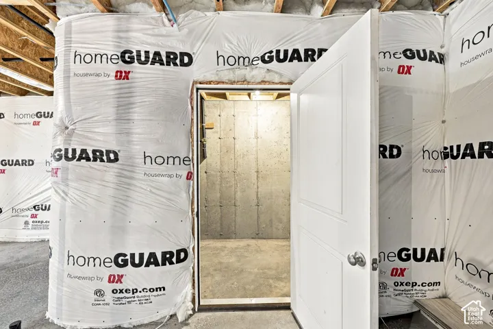Unfinished basement space featuring exposed wood framing, insulation wrap, concrete slab flooring, and a white interior door