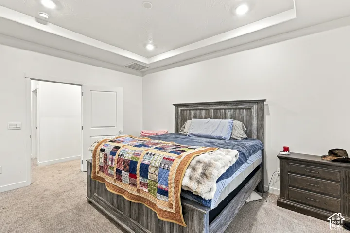Recessed tray ceiling with integrated lighting, neutral carpeting, and a rustic wood-finish bed frame