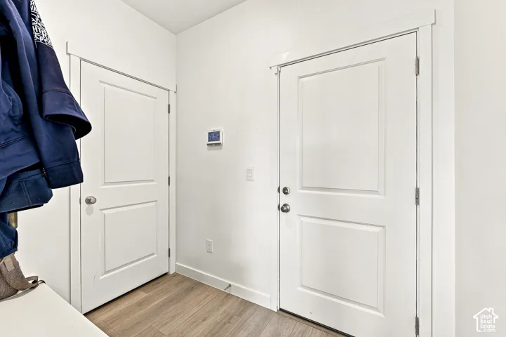 Entryway featuring two paneled doors with brushed nickel hardware, wood-finish flooring, white baseboards, and a wall-mounted thermostat