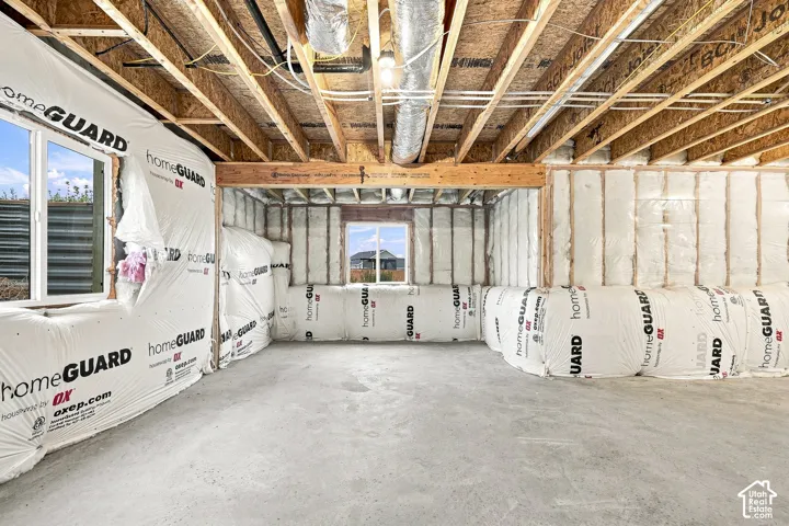 Unfinished basement featuring exposed wood joists and subflooring, insulated walls with HomeGUARD wrap, concrete flooring, and multiple windows providing natural light
