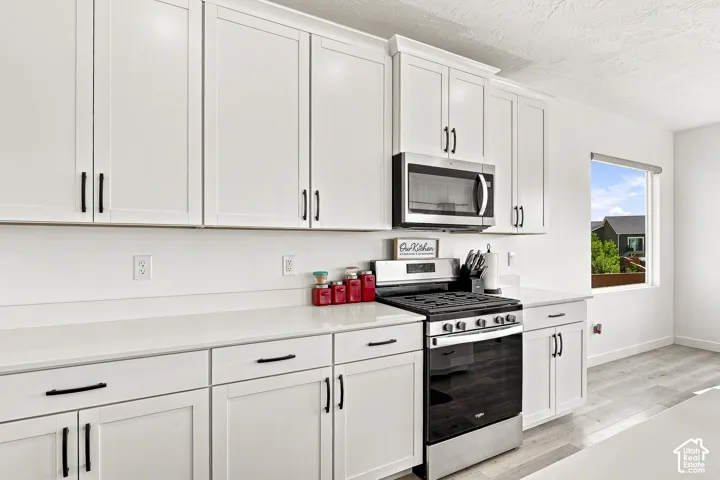 Modern kitchen featuring white shaker cabinetry, stainless steel appliances, light-toned countertops, and light wood-finish flooring