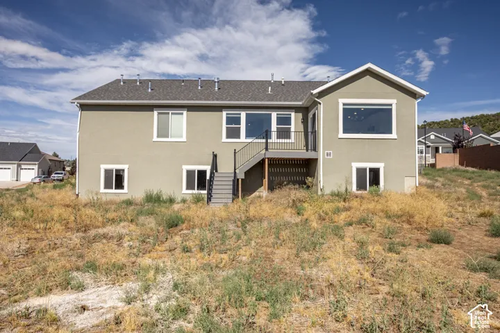 Rear exterior featuring a neutral stucco facade and a gray shingle roof