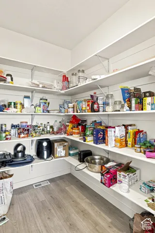 Walk-in pantry featuring extensive white shelving, wood-finish flooring, and white baseboards
