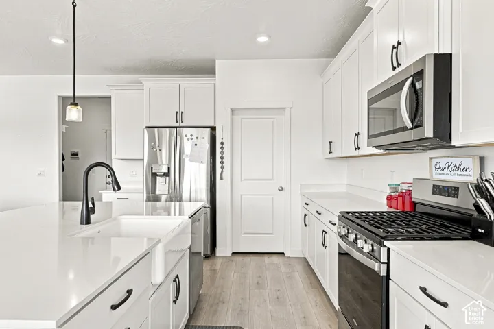 Kitchen featuring white shaker cabinetry, white countertops, a deep farmhouse sink with a matte black faucet, stainless steel appliances, and wood-finish flooring