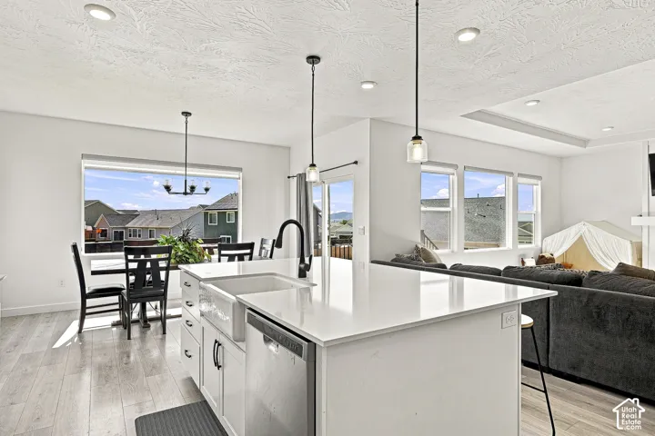 Open-concept kitchen and dining area featuring a large center island with a farmhouse sink, light wood-finish flooring, recessed lighting, and a prominent window