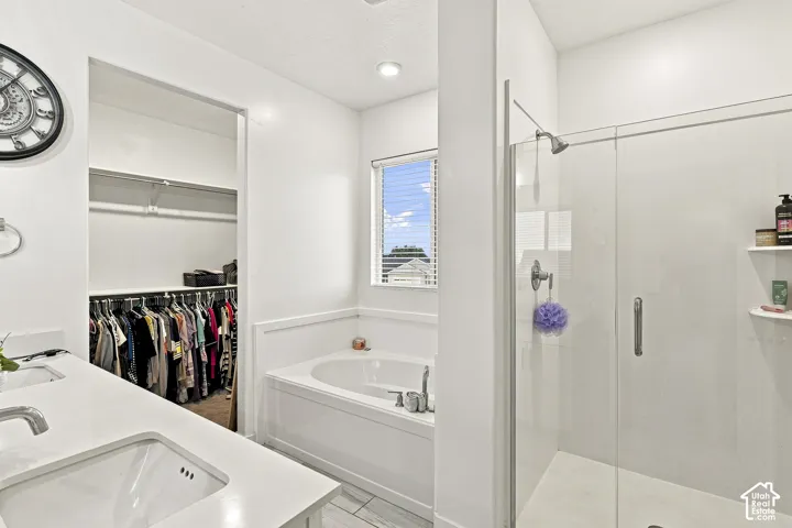 Bathroom featuring a glass-enclosed shower, a built-in soaking tub, a single vanity with an integrated sink, a window, and an open closet