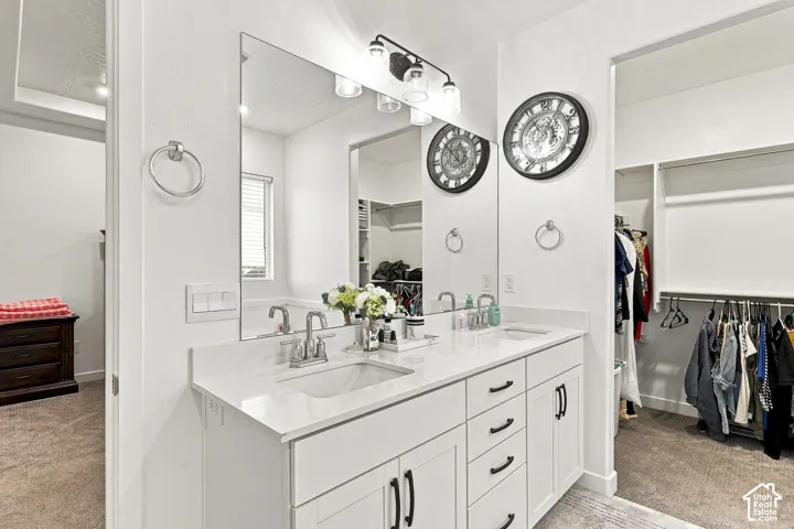 Double vanity featuring white cabinetry, integrated sinks, chrome fixtures, and a large wall mirror