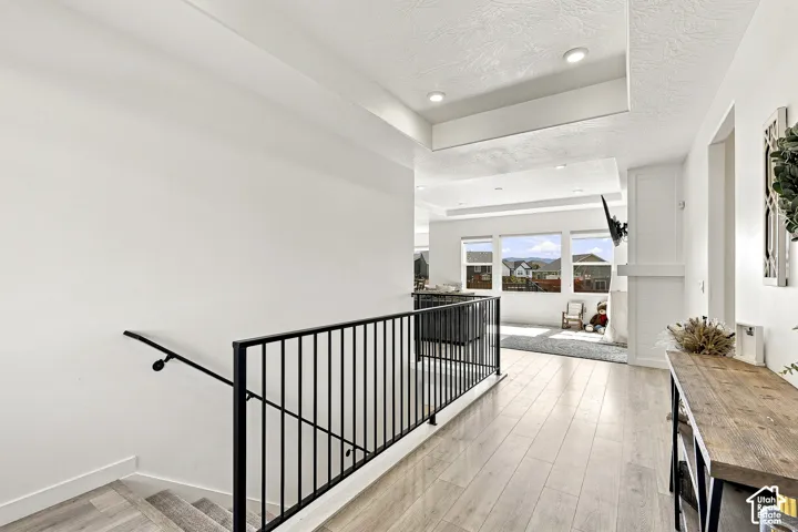Open-concept living space featuring light wood-finish flooring, recessed lighting, white walls, and a black metal staircase railing