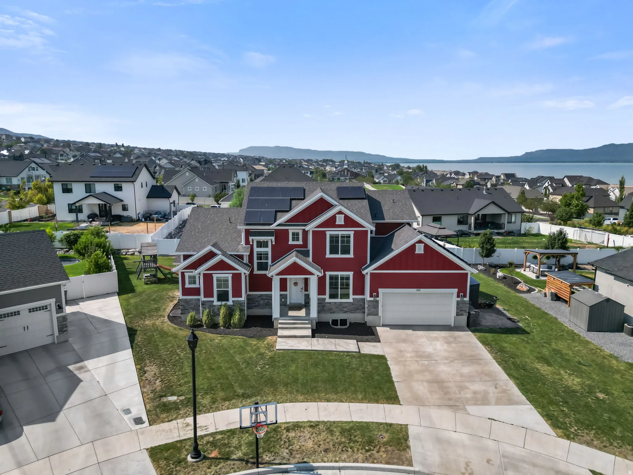 Red exterior with white trim, stone accents, two-car garage, solar panels, and a landscaped front yard